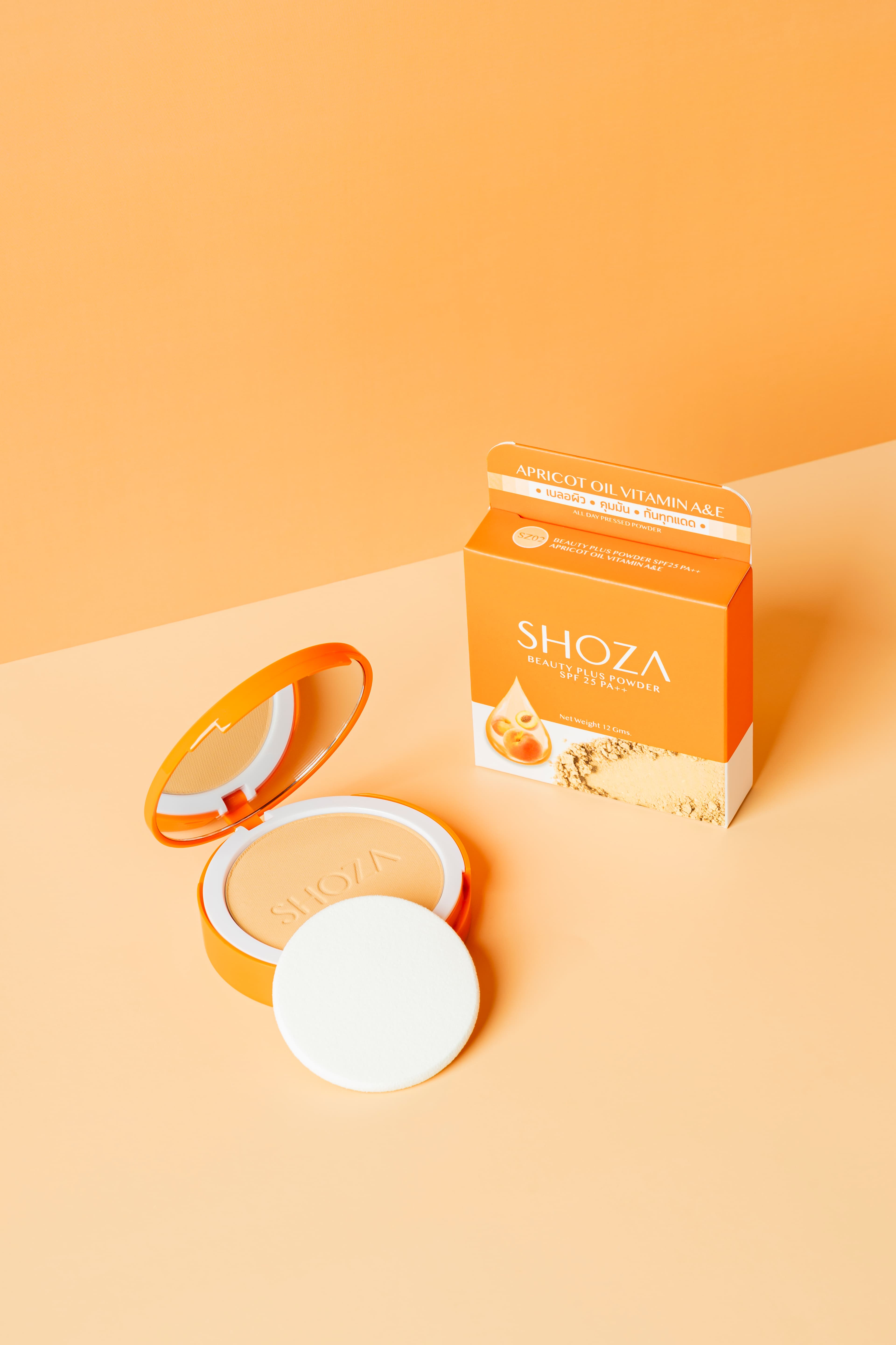 ตลับแป้ง SHOZA Beauty Plus Powder เปิดฝาพร้อมพัฟ วางคู่กล่องบรรจุภัณฑ์สีส้ม Apricot Oil Vitamin A&E