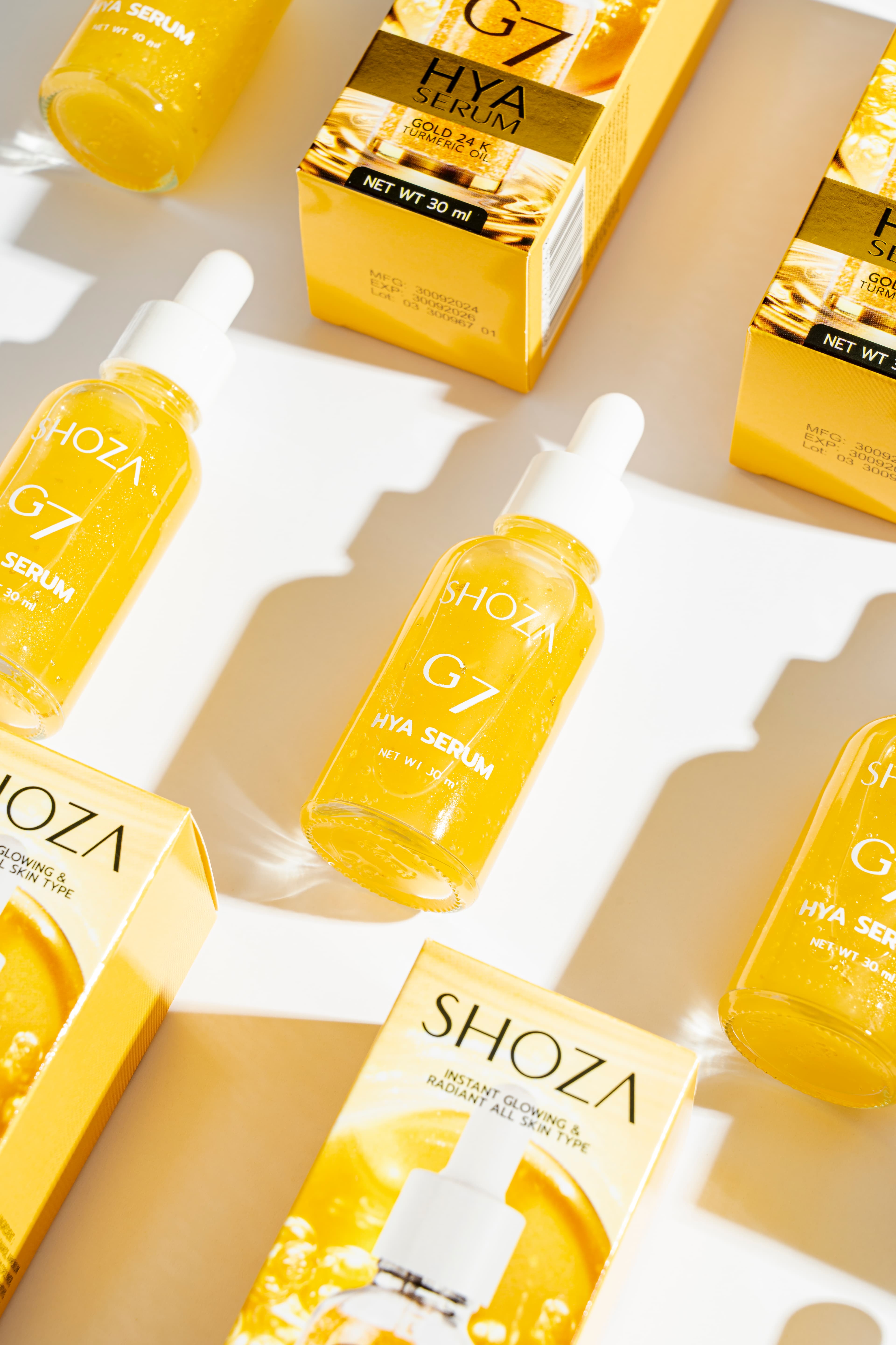 ขวดเซรั่ม SHOZA G7 Hya Serum สีทองพร้อมกล่องบรรจุภัณฑ์ วางเรียงเป็นแฟลตเลย์รับแสงแดด